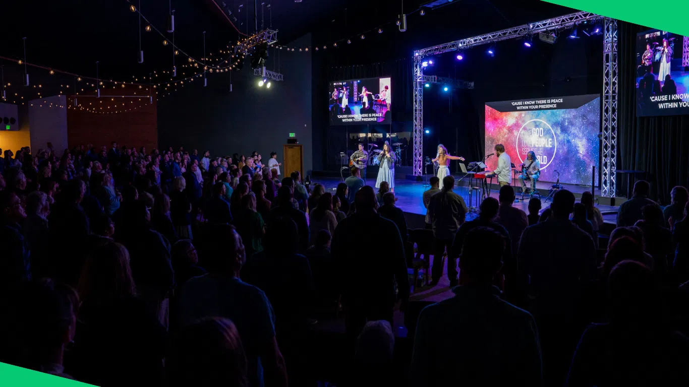A turnkey live production setup in a church sanctuary — a massive central LED wall and flanking side screens light a high-energy worship environment with integrated stage lighting, immersive for both the in-person congregation and the livestream audience.